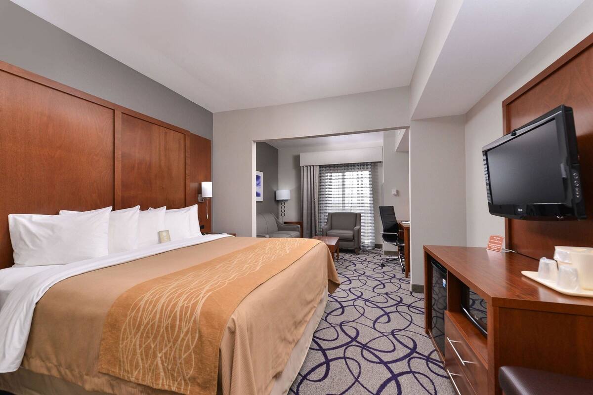 A hotel room with a large bed, a desk with a television, and a bathroom visible through an open door.