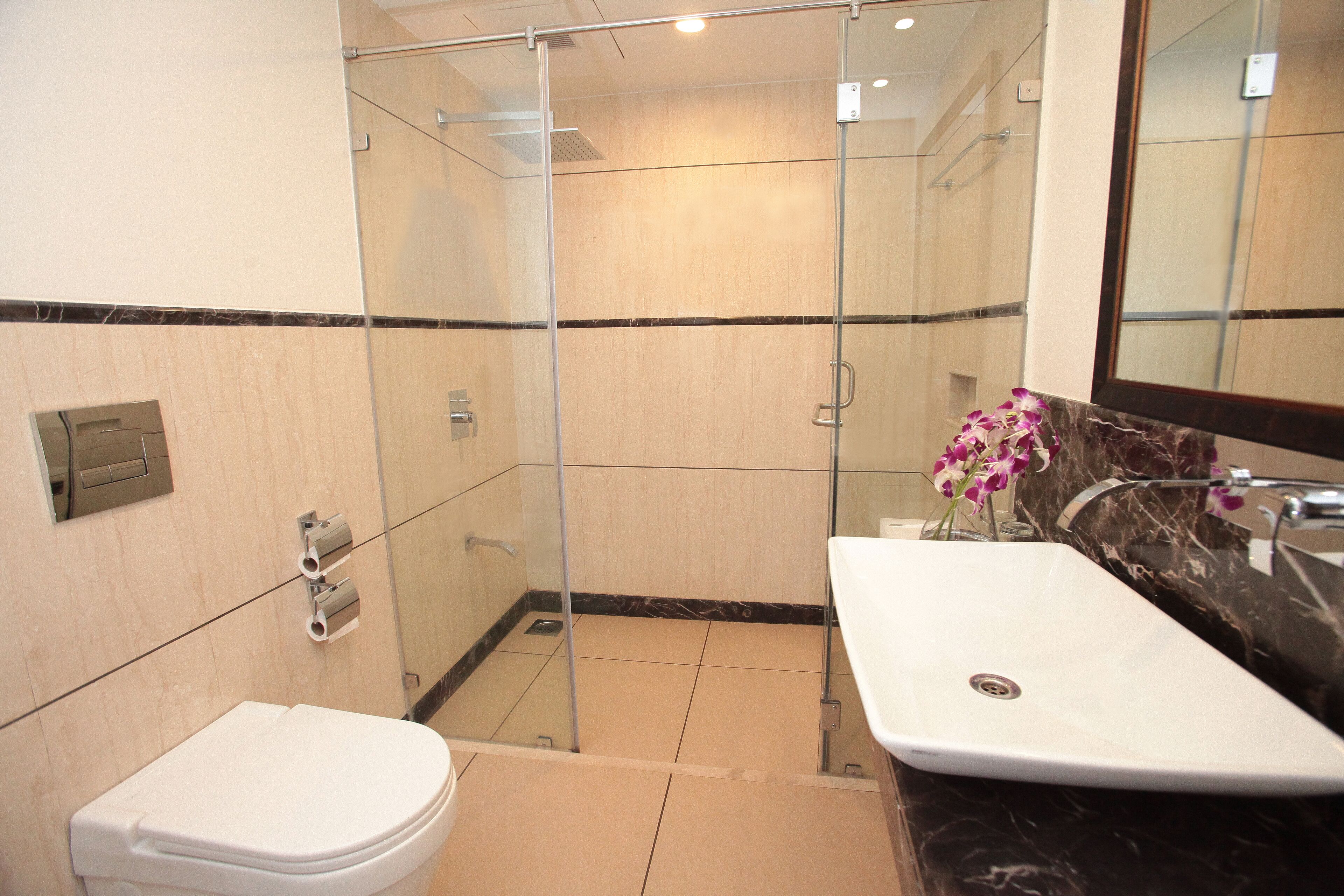 A bathroom with a glass-enclosed shower, a white sink with a marble countertop, and a toilet.