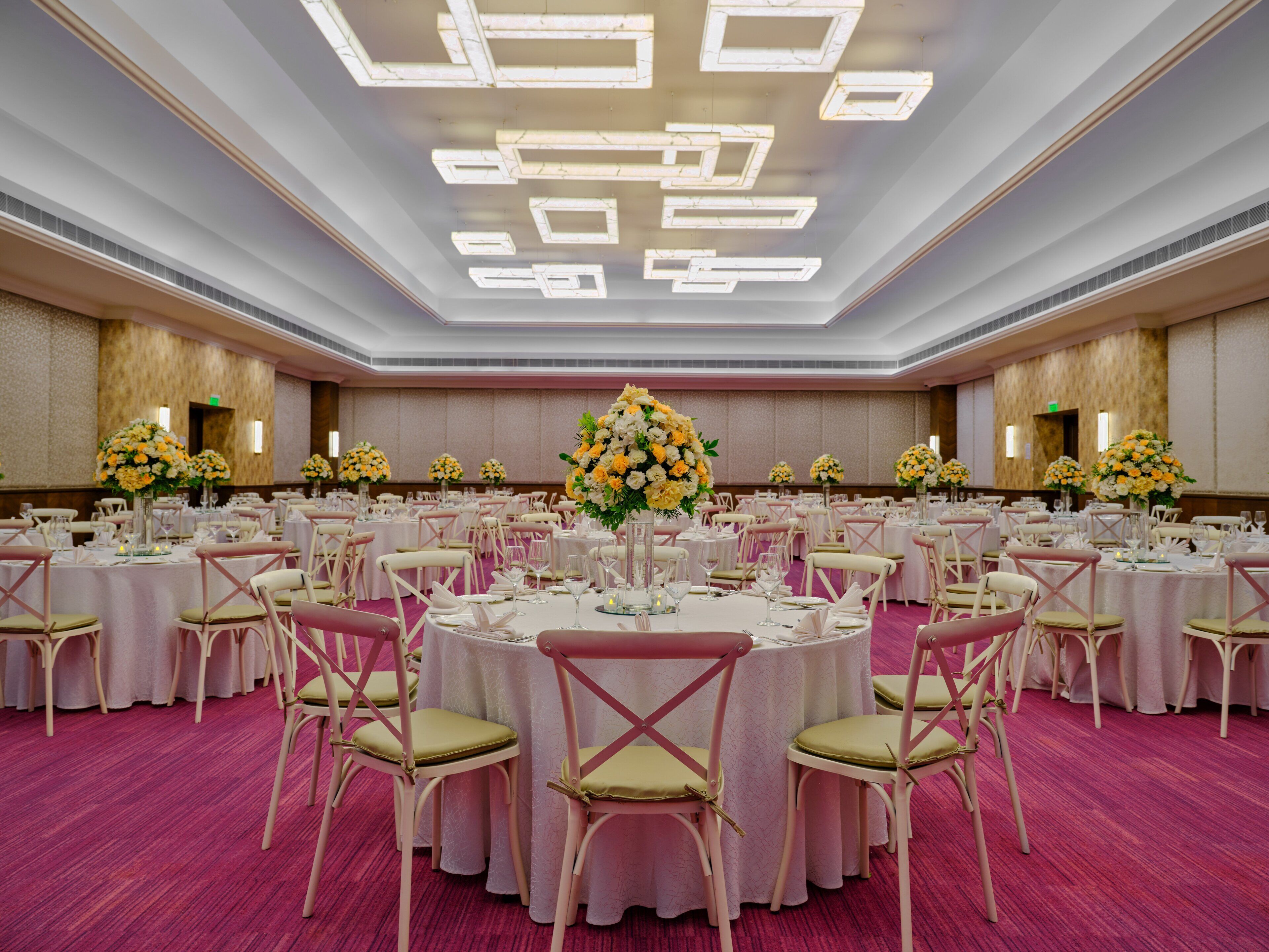 A large banquet hall with round tables, chairs, and floral centerpieces.