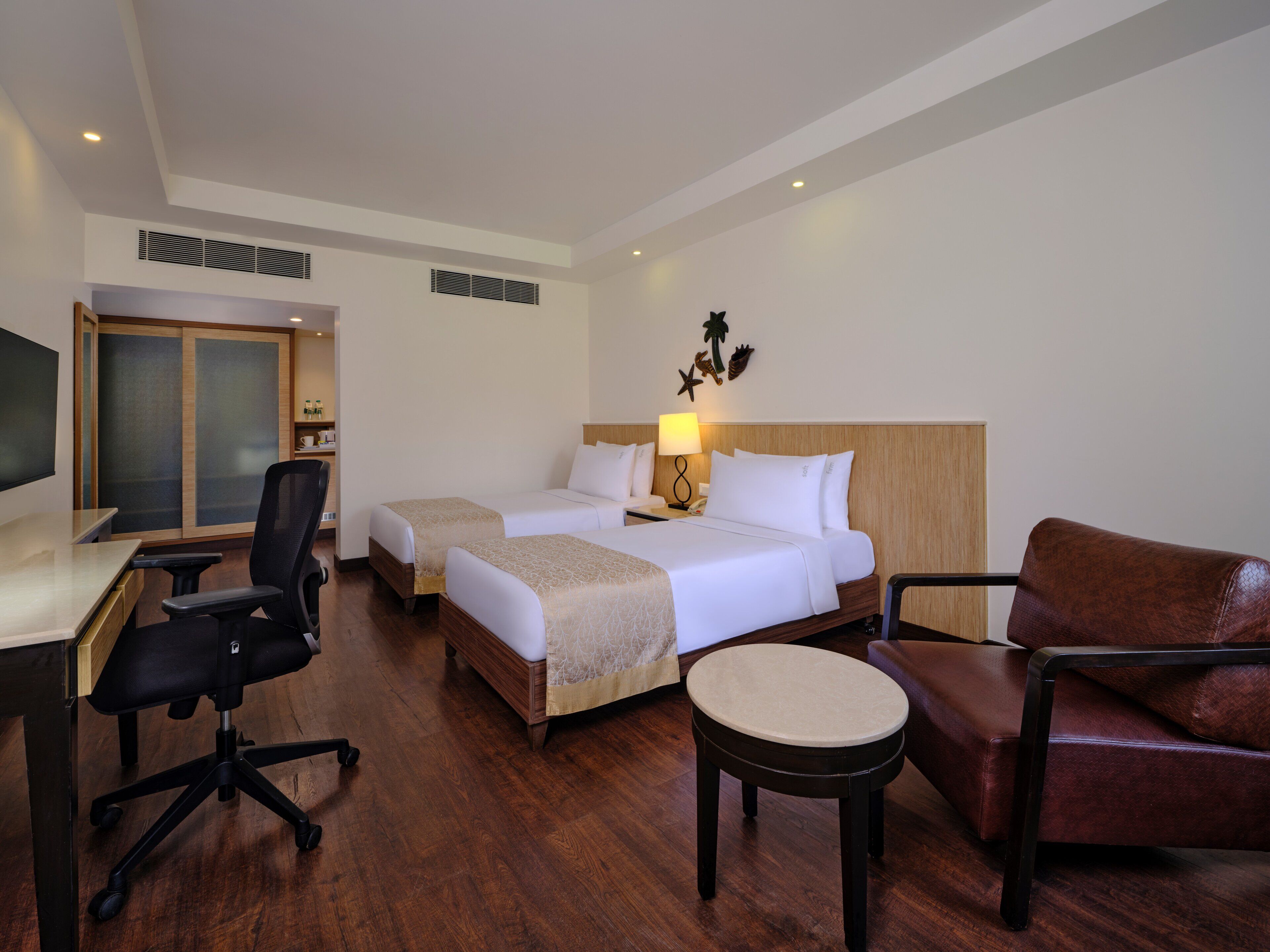 A hotel room with two beds, a desk, a chair, a small table, and a TV.