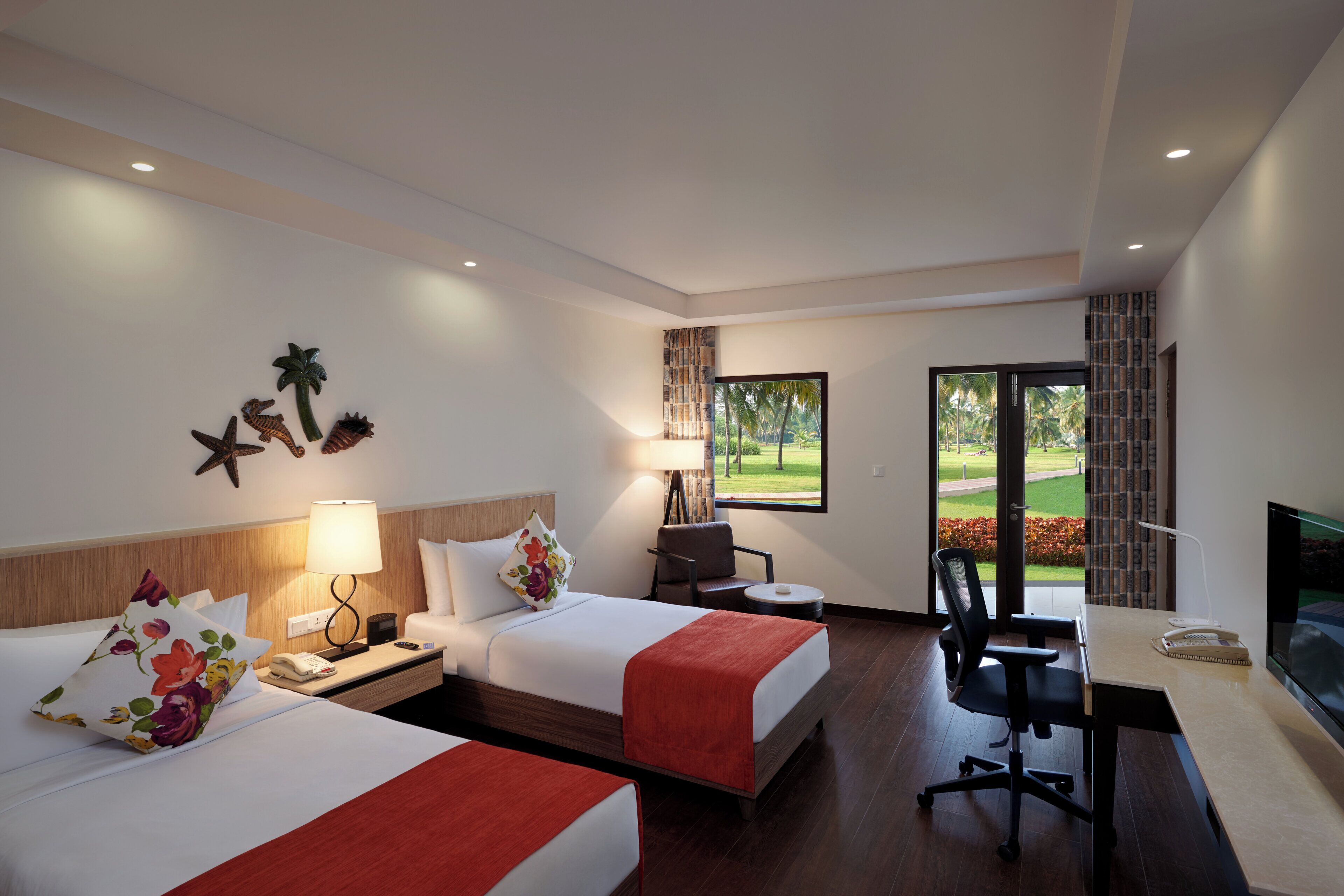 A hotel room with two beds, a desk, a chair, a TV, and a window with a view of a garden.
