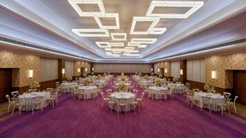 Un amplio salón de banquetes con mesas redondas y sillas dispuestas en filas, y un suelo cubierto de moqueta morada.