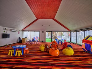 A spacious indoor play area with a high ceiling, colorful play equipment, and a large window offering a view of the outdoors.