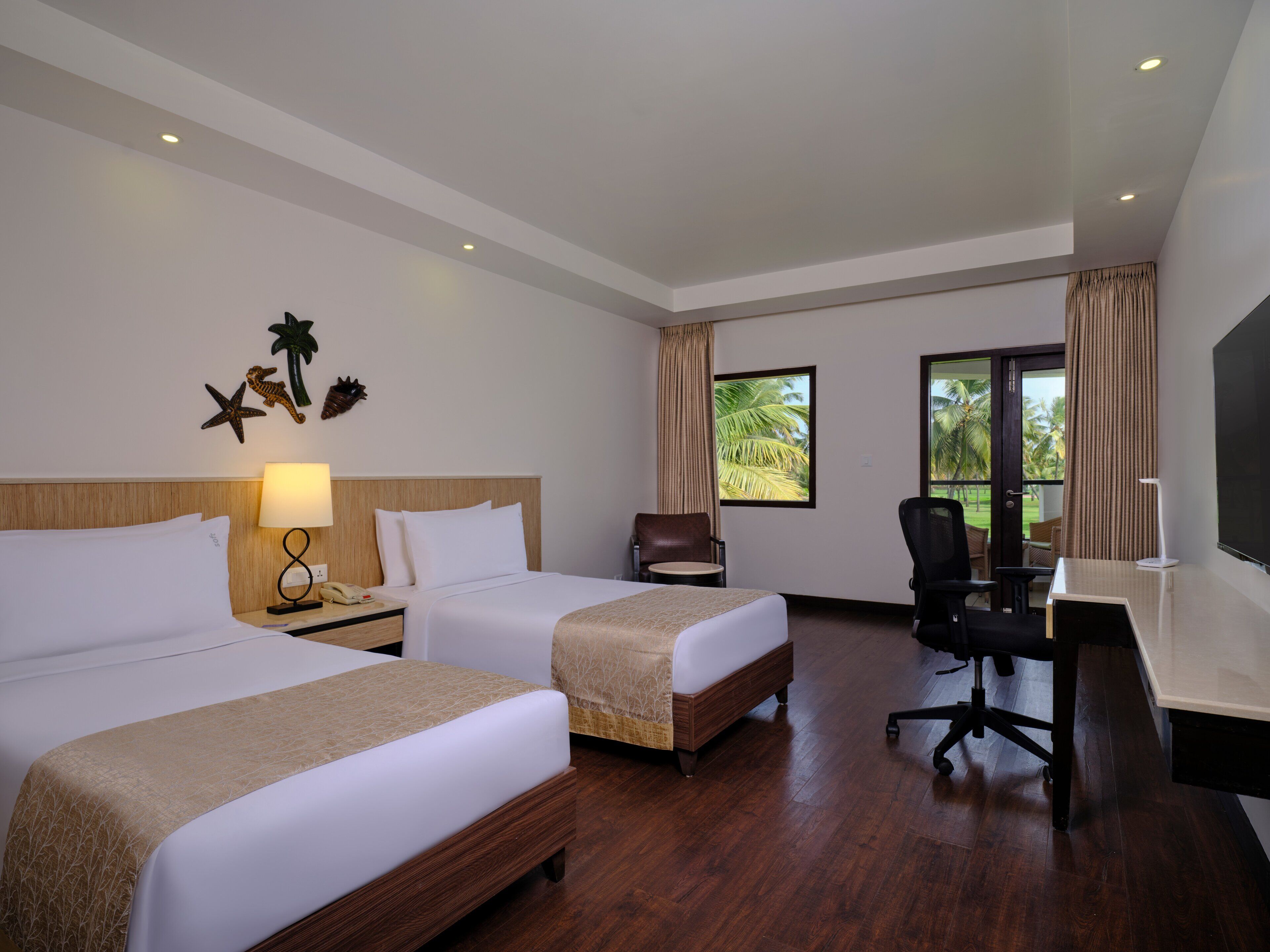 A hotel room with two beds, a desk, a chair, a TV, and a window with a view of palm trees.