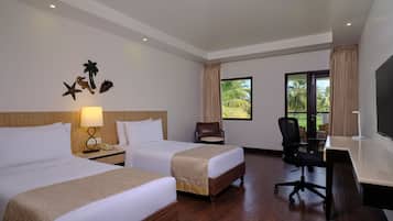 A hotel room with two beds, a desk, a chair, a TV, and a window with a view of palm trees.