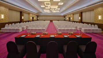 A conference room with rows of white chairs, a long table with nameplates, and a red carpet.