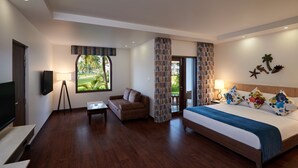 A hotel room with a bed, a sofa, a TV, and a window with a view of greenery. - Holiday Inn Resort Goa by IHG (Cavelossim)