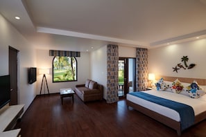 A hotel room with a bed, a sofa, a TV, and a window with a view of greenery.
