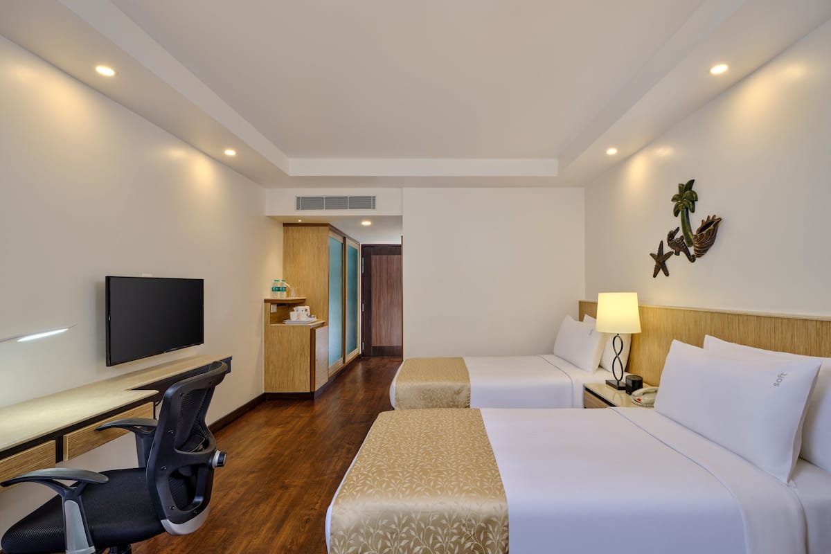 A hotel room with a desk, two beds, a TV, a small kitchenette, and a decorative wall piece.