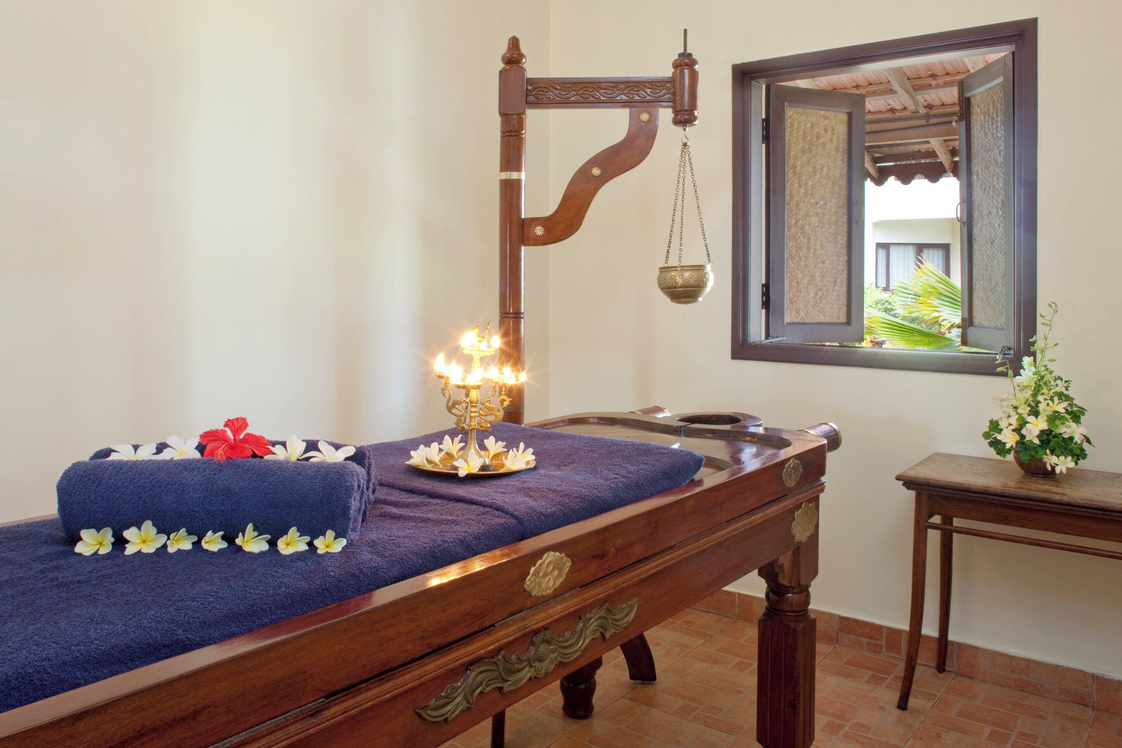 A wooden massage table with a blue towel and decorative flowers, a hanging lamp, and a small table with a plant.