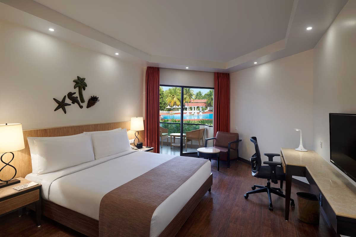 A hotel room with a large bed, a desk with a chair, a TV, and a view of a swimming pool.