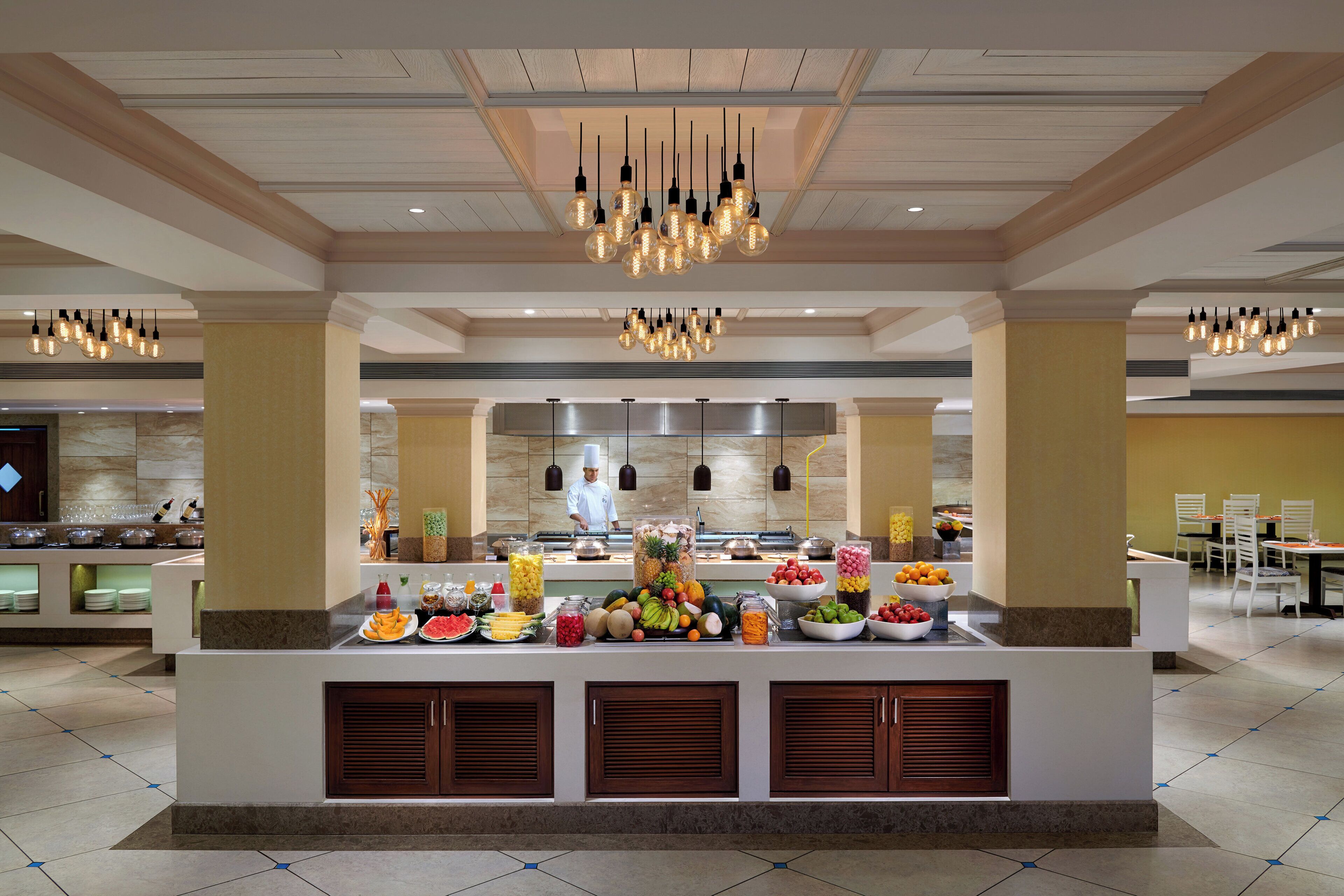 A buffet setup with a chef preparing food, surrounded by various food items and a modern interior design.