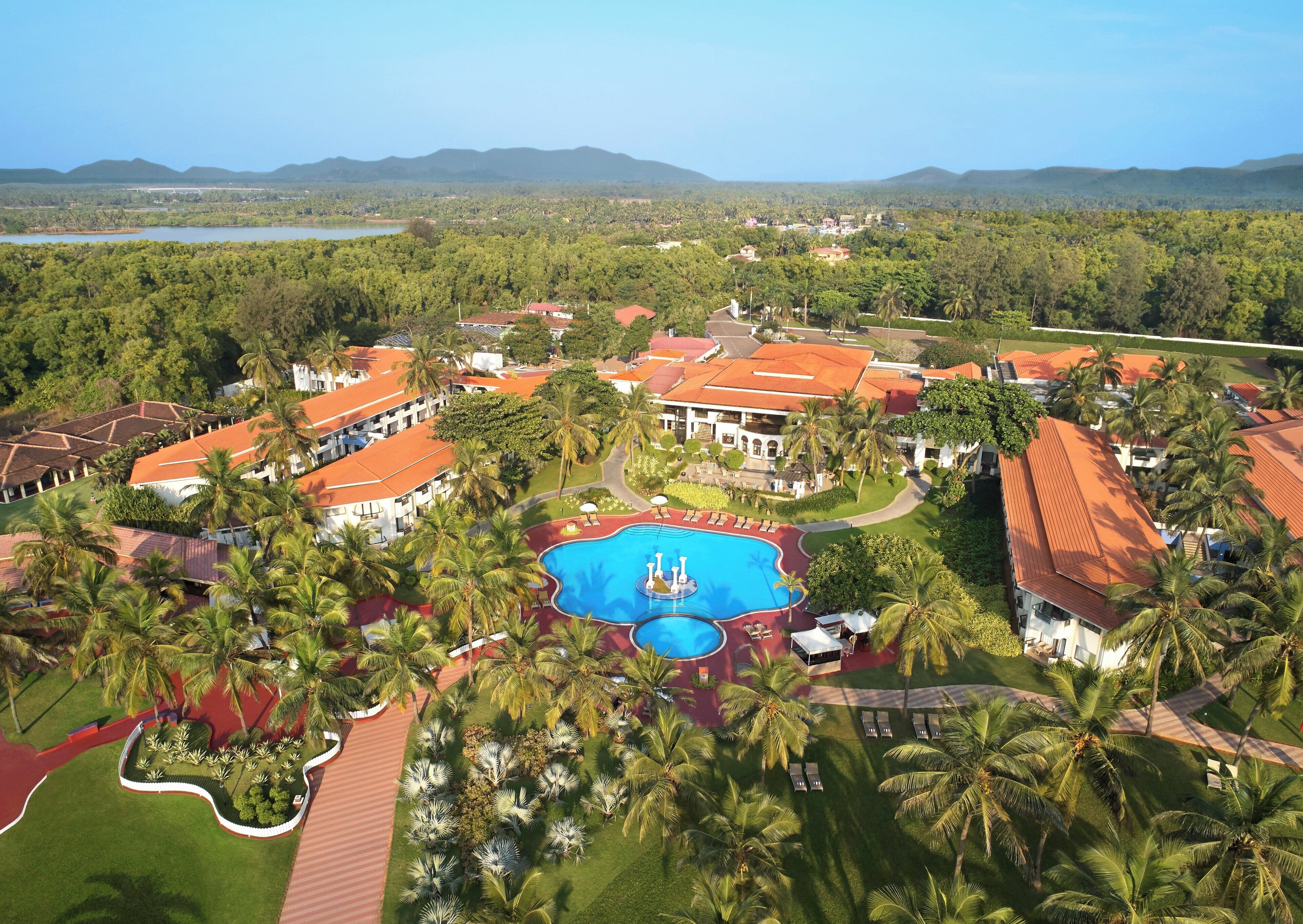 A resort with a central swimming pool, surrounded by palm trees and red-roofed buildings.
