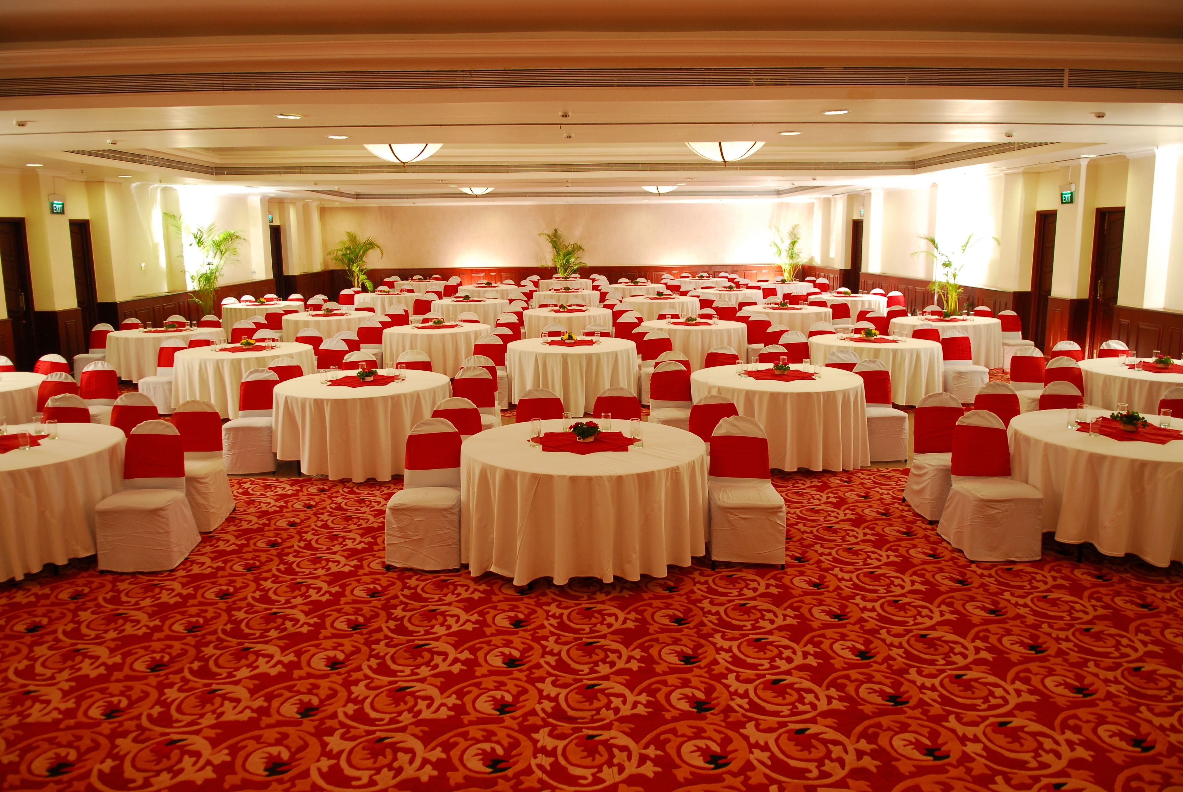 Un salón de banquetes con mesas redondas, sillas rojas y blancas, y un suelo cubierto de moqueta roja.