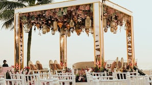 A beach wedding setup with a white gazebo, chairs, and floral decorations.