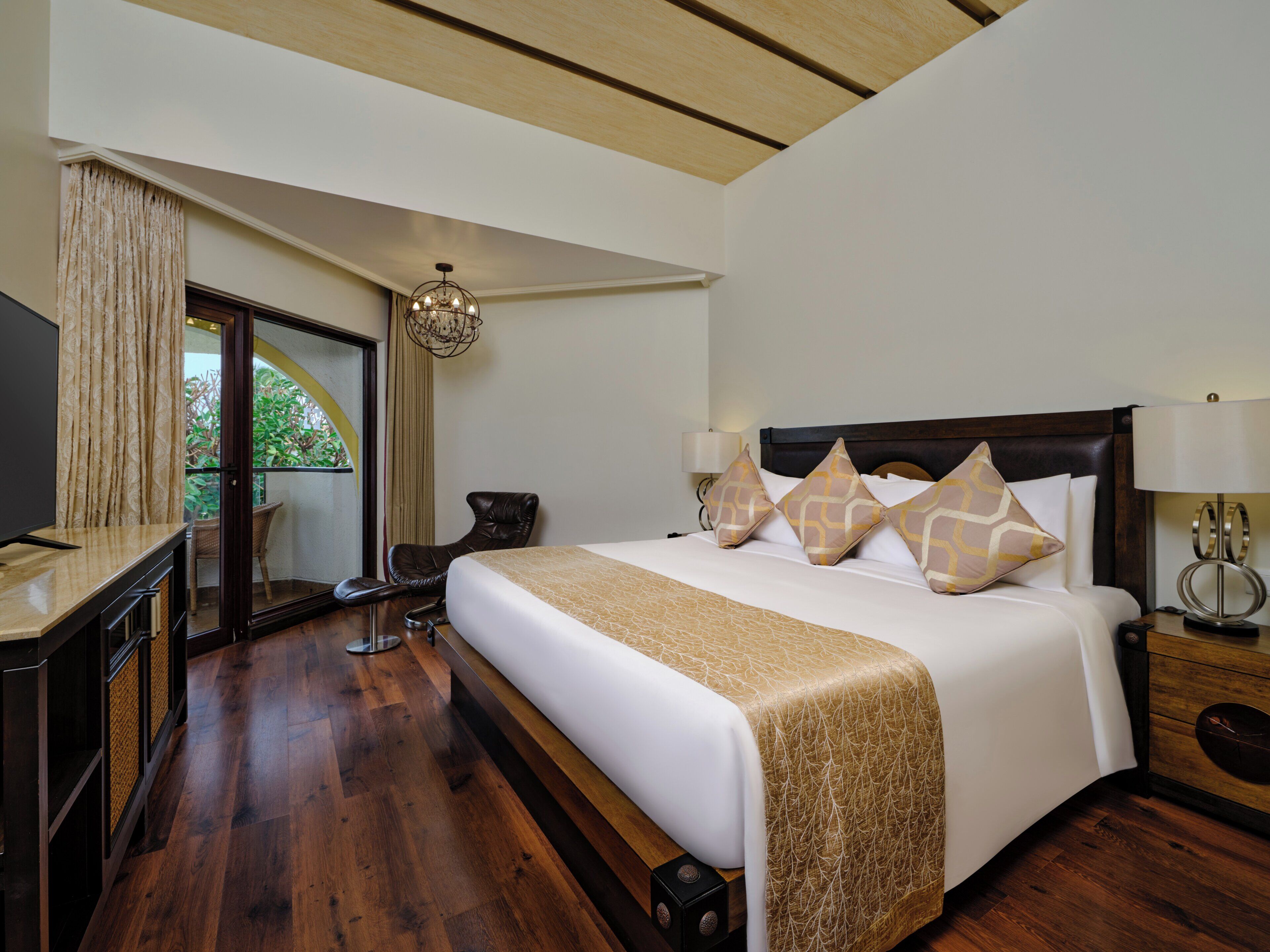 Une chambre d’hôtel avec un grand lit, un bureau, une chaise, une télévision et une vue sur la verdure par la fenêtre.
