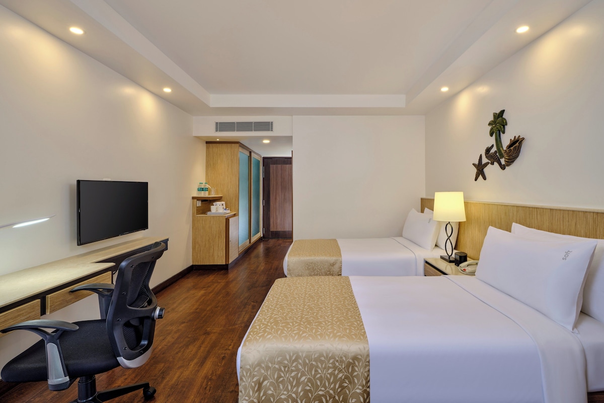 A hotel room with a desk, two beds, a TV, a small kitchenette, and a decorative wall piece.
