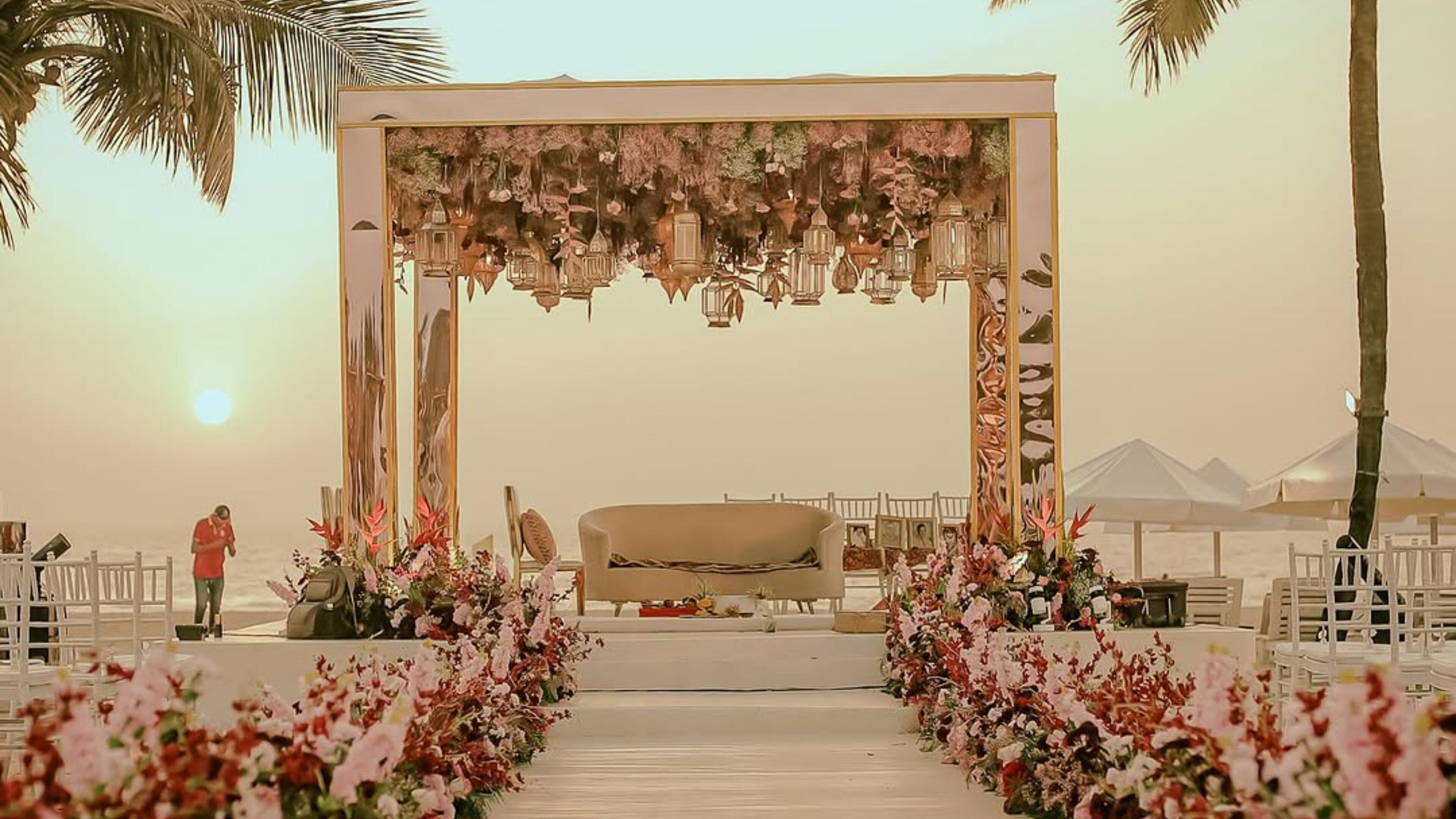 Decoración para una ceremonia de boda con un arco floral, un sofá y un sendero bordeado de flores.