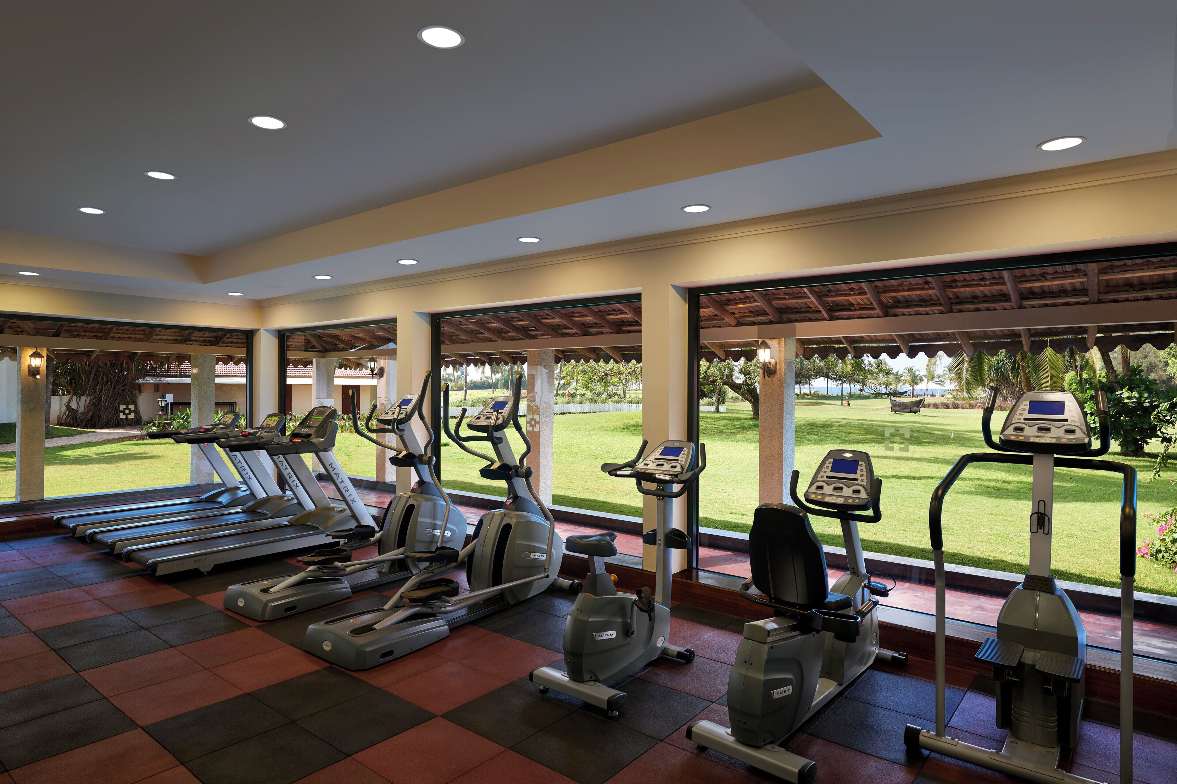 Ein Fitnessstudio mit Laufbändern, Crosstrainern und Rudergeräten, mit Blick auf einen Golfplatz durch große Fenster.