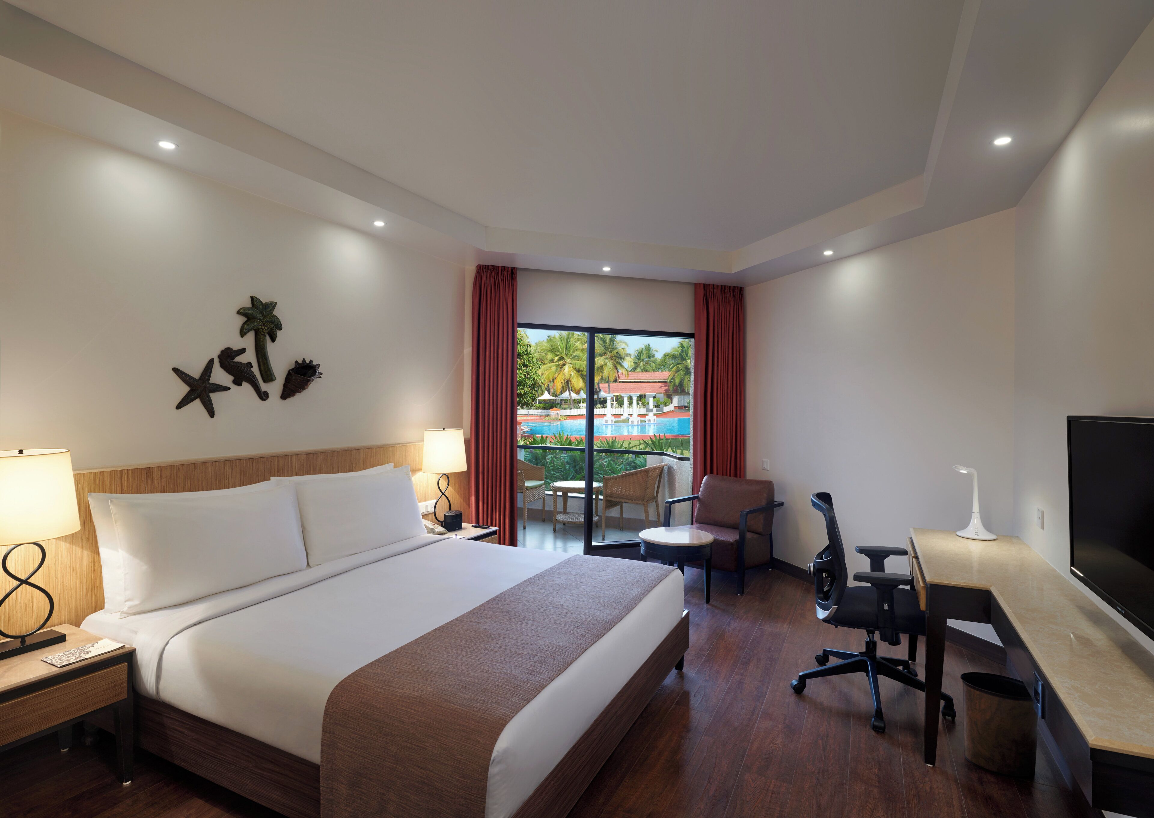 Quarto de hotel com cama, escrivaninha, cadeira e vista para uma piscina ao ar livre.