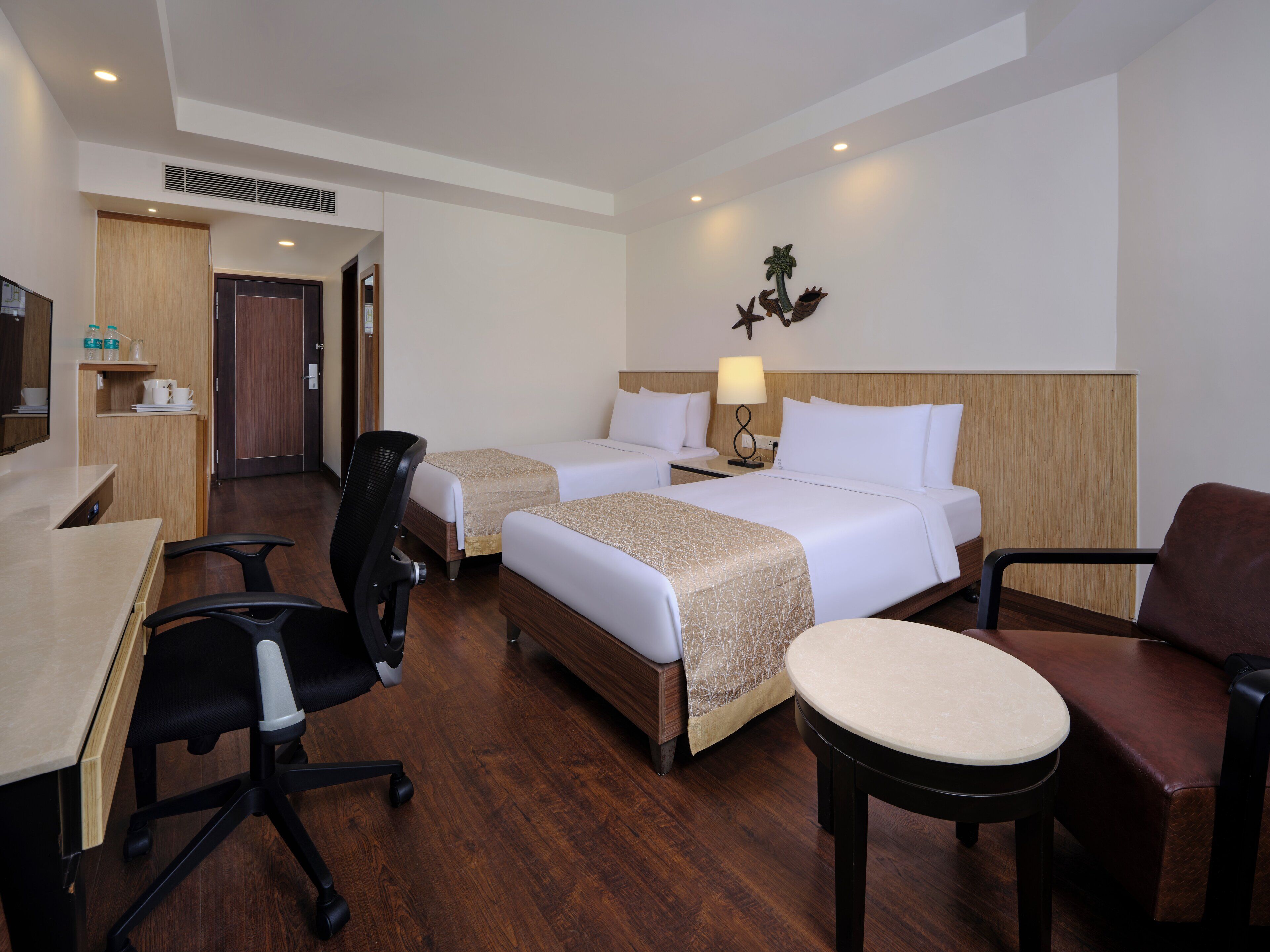 A hotel room with two beds, a desk, a chair, and a small table.