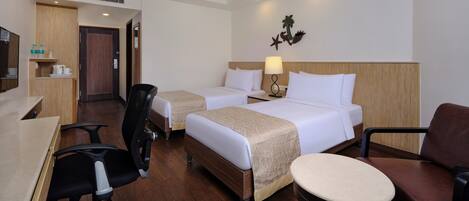A hotel room with two beds, a desk, a chair, and a small table.