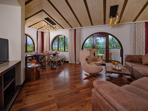 A spacious living area with wooden flooring, a dining table set for four, a large curved armchair, and a sofa.