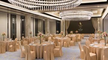 Un salón de banquetes con mesas redondas, sillas color beige y una gran lámpara de araña.