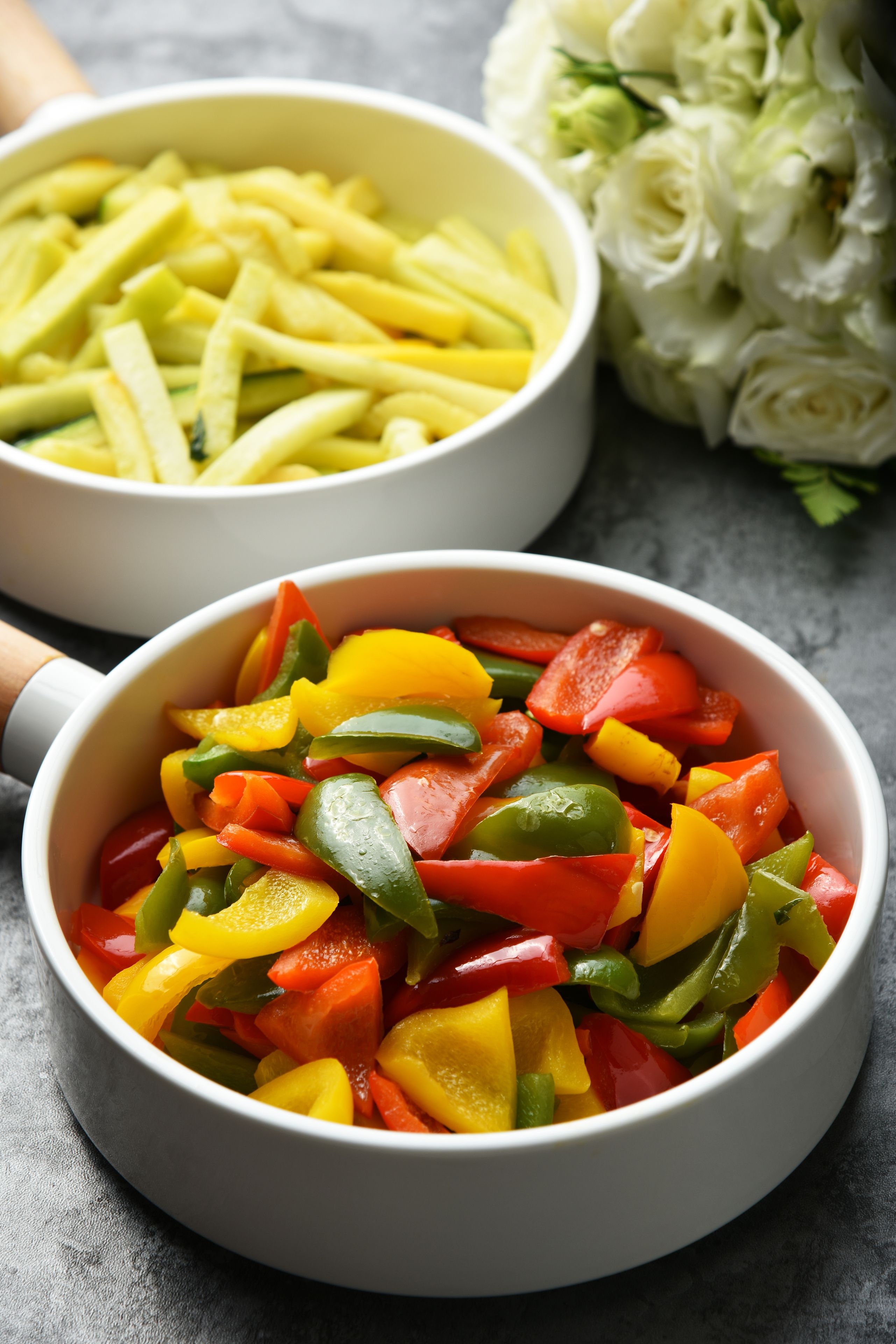 Deux bols de légumes coupés en tranches : l’un contient des poivrons jaunes et verts, et l’autre, des poivrons rouges et jaunes. Les bols sont posés sur une surface grise.