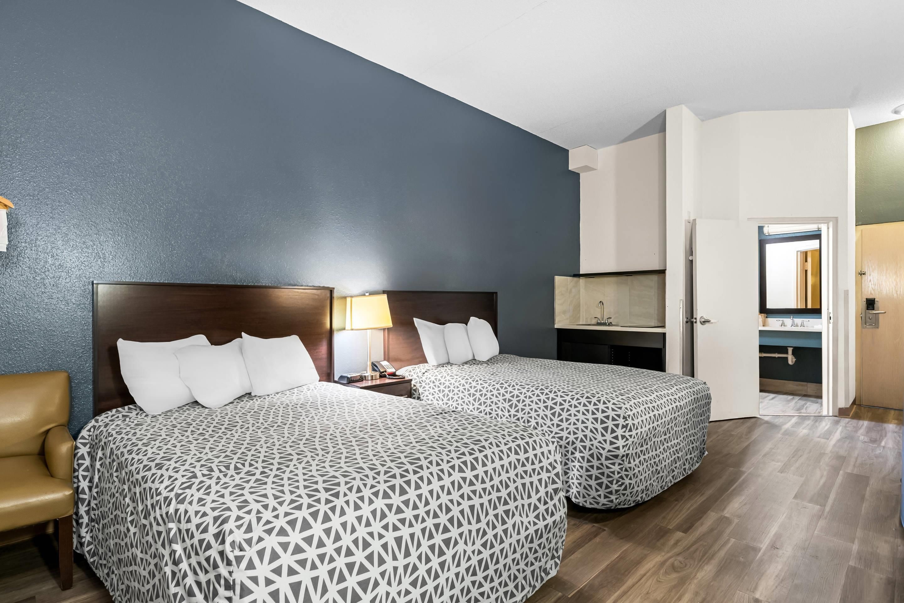 A hotel room with two beds, a desk, a chair, and a bathroom visible through an open door.