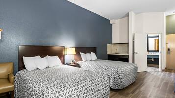 A hotel room with two beds, a desk, a chair, and a bathroom visible through an open door.