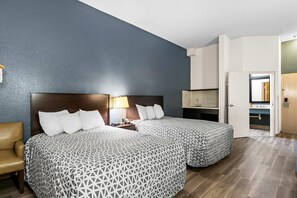 Habitación de hotel con dos camas, un escritorio, una silla y un baño visible a través de una puerta abierta.