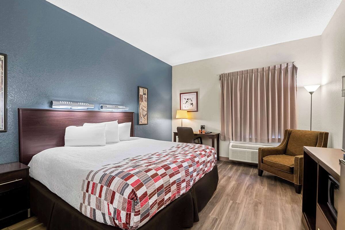Une chambre d’hôtel avec un grand lit, un bureau, une chaise, une lampe et une fenêtre avec des rideaux.