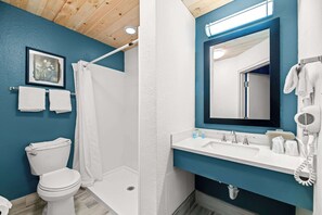 Un baño con inodoro blanco, ducha, lavabo con espejo y secador de pelo.