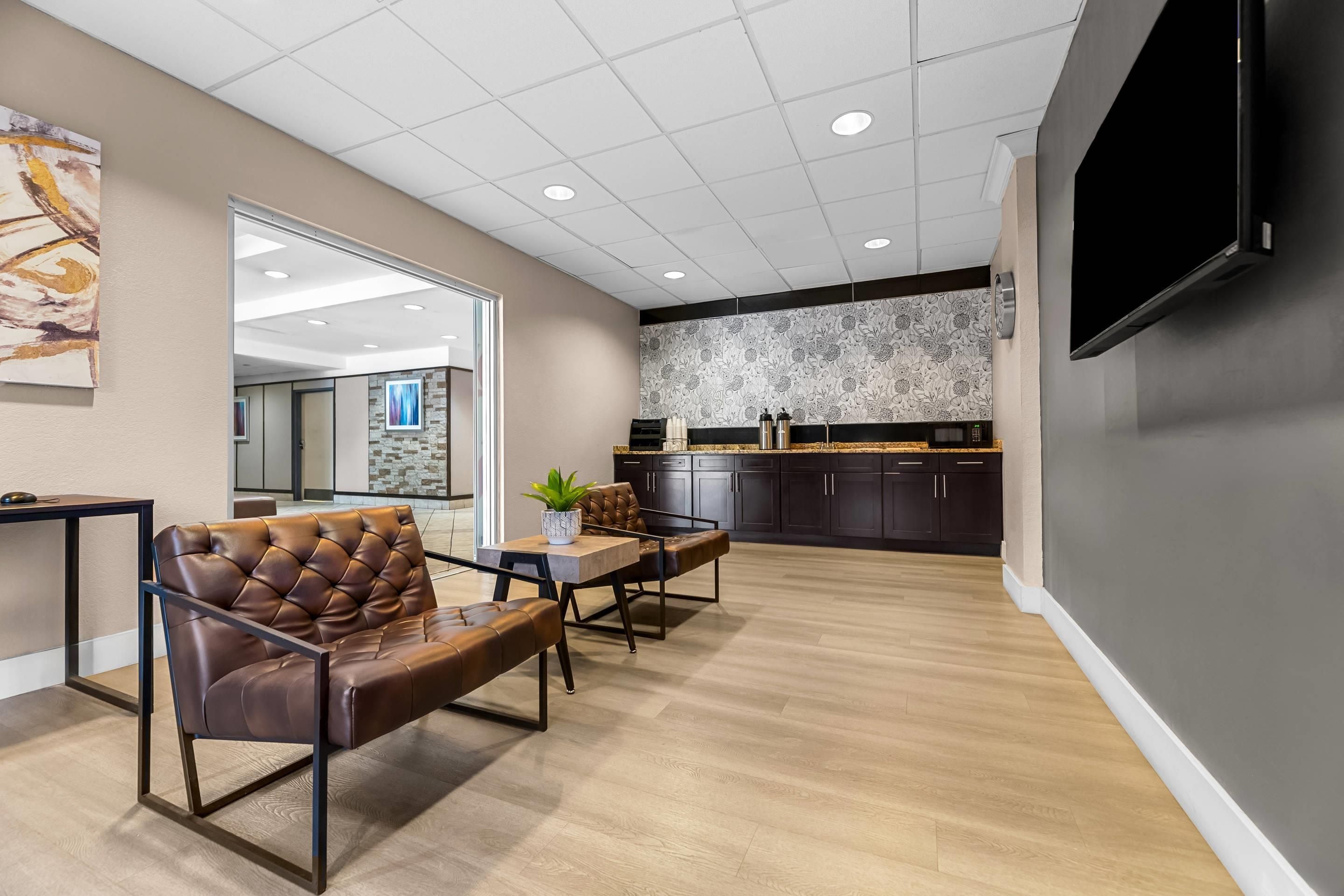 A modern interior with a seating area, a kitchen, and a large flat-screen TV mounted on the wall.