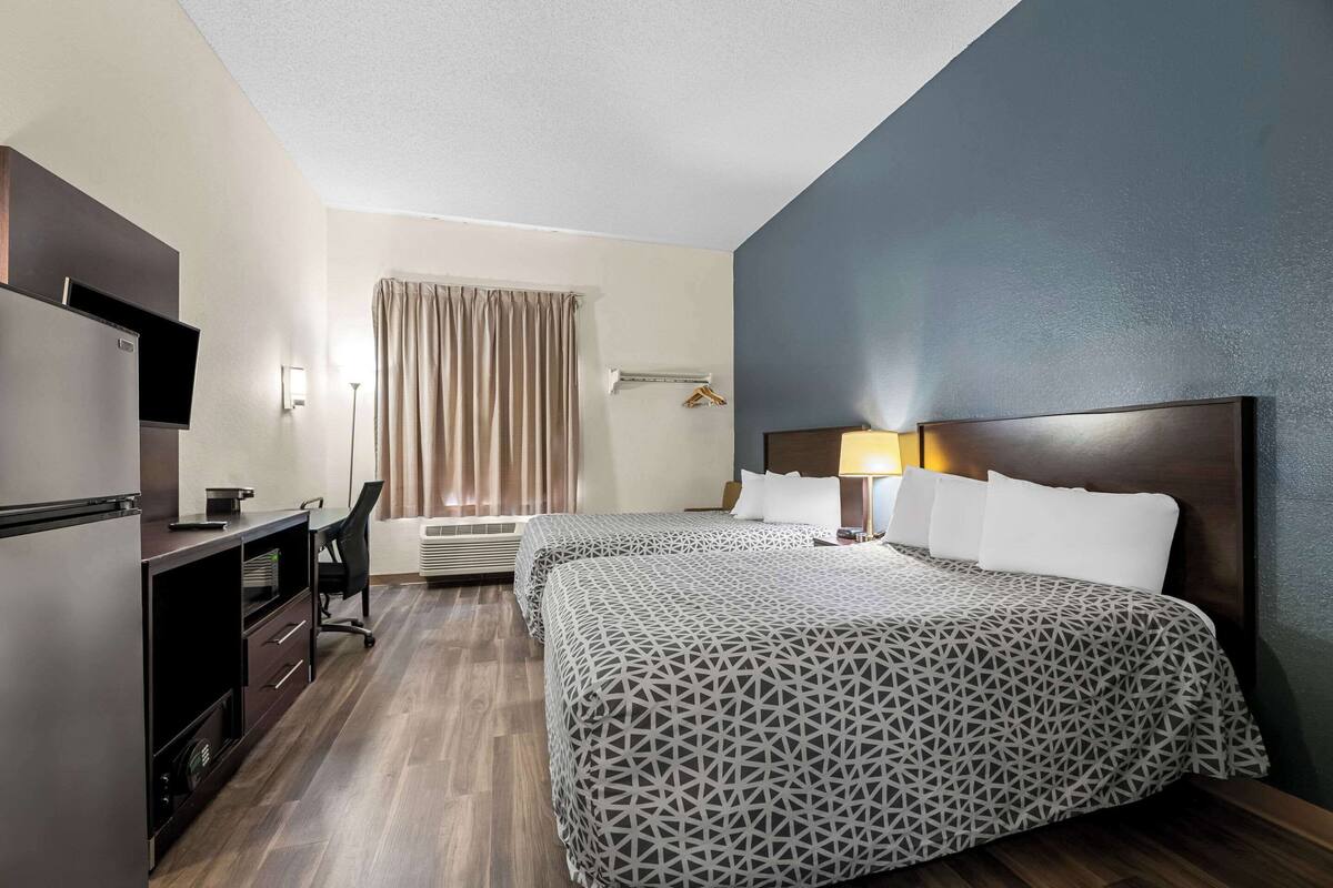 Une chambre d’hôtel avec deux lits, un bureau avec une chaise, une télévision et une fenêtre avec des rideaux.