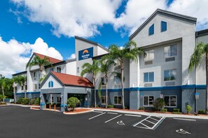 Un hotel con diseño moderno, que presenta un llamativo letrero de 'Suburban Studios', un acceso cubierto y un estacionamiento con acceso para discapacitados.