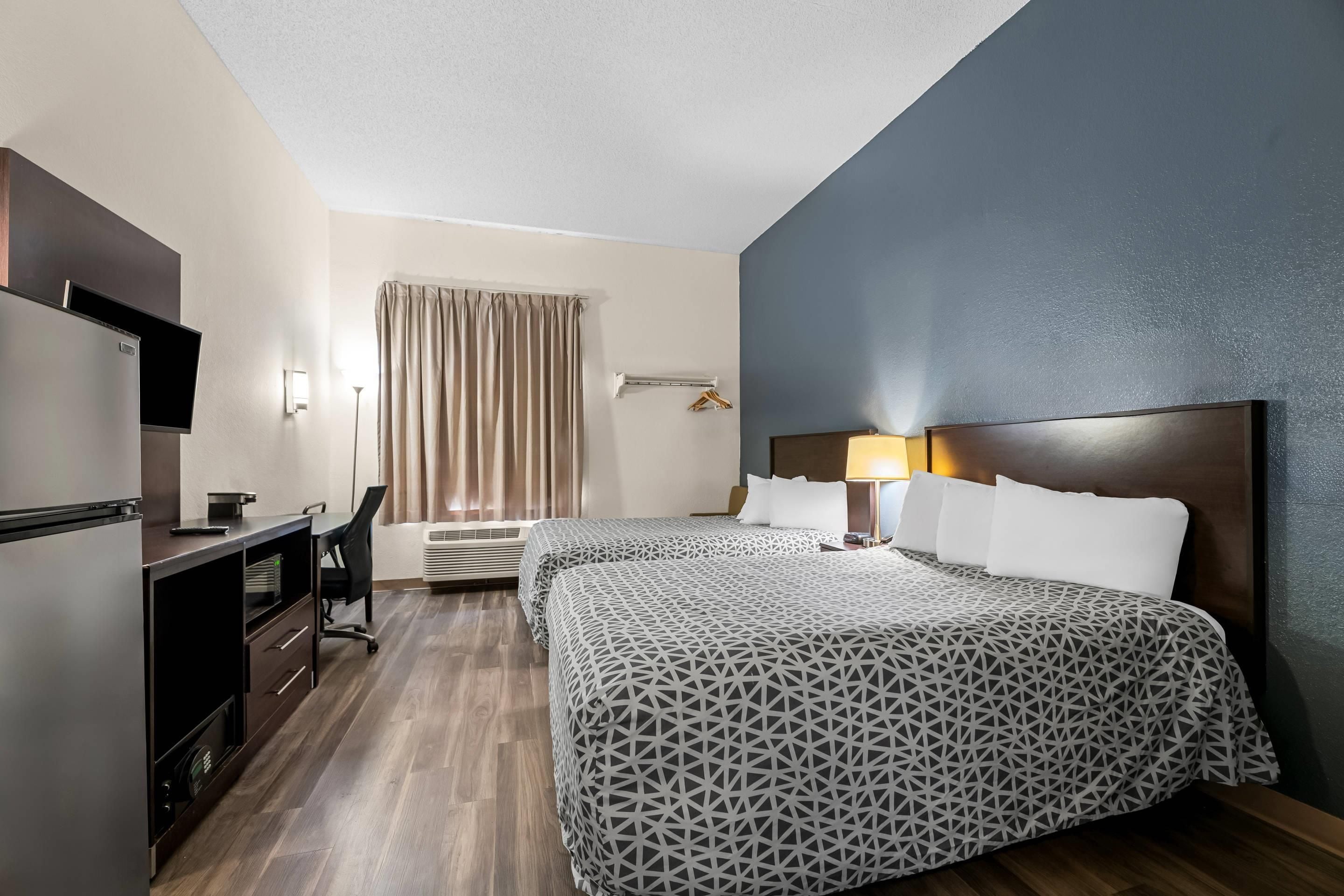 A hotel room with two beds, a desk, a television, and a window with curtains.