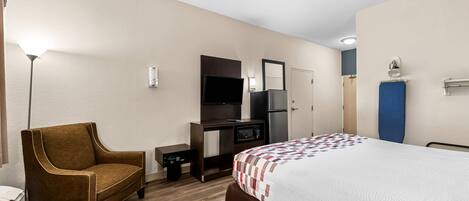 Habitación de hotel con cama, escritorio, silla, microondas, refrigerador y televisor de pantalla plana.