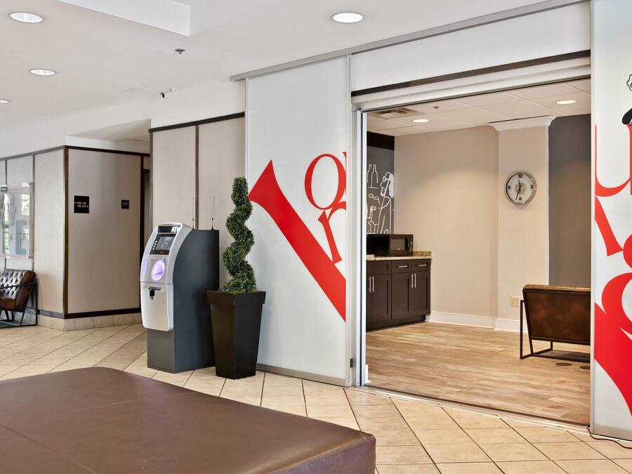 A modern hotel lobby with a reception desk, a self-service kiosk, and a seating area.