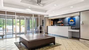 A hotel lobby with a reception desk, a brown leather bench, and a large window with a view of greenery.