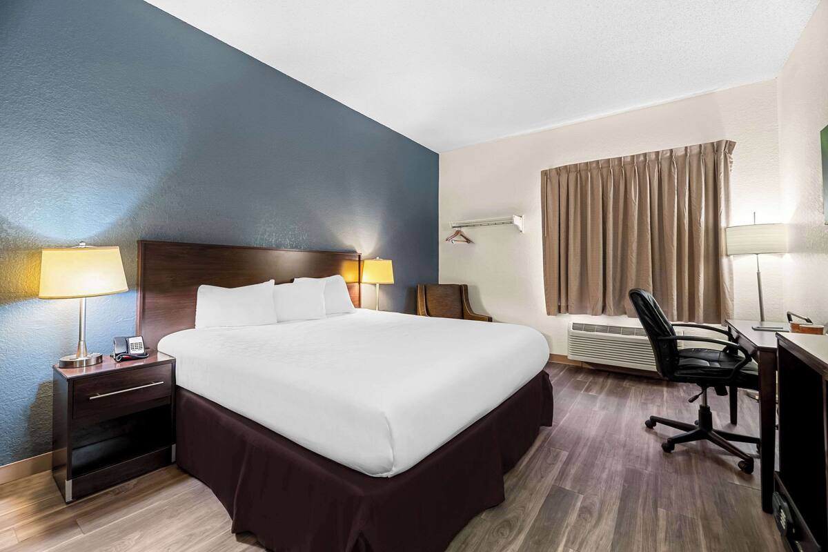 Une chambre d’hôtel avec un grand lit, des lampes de chevet, un bureau avec une chaise et une fenêtre avec des rideaux.