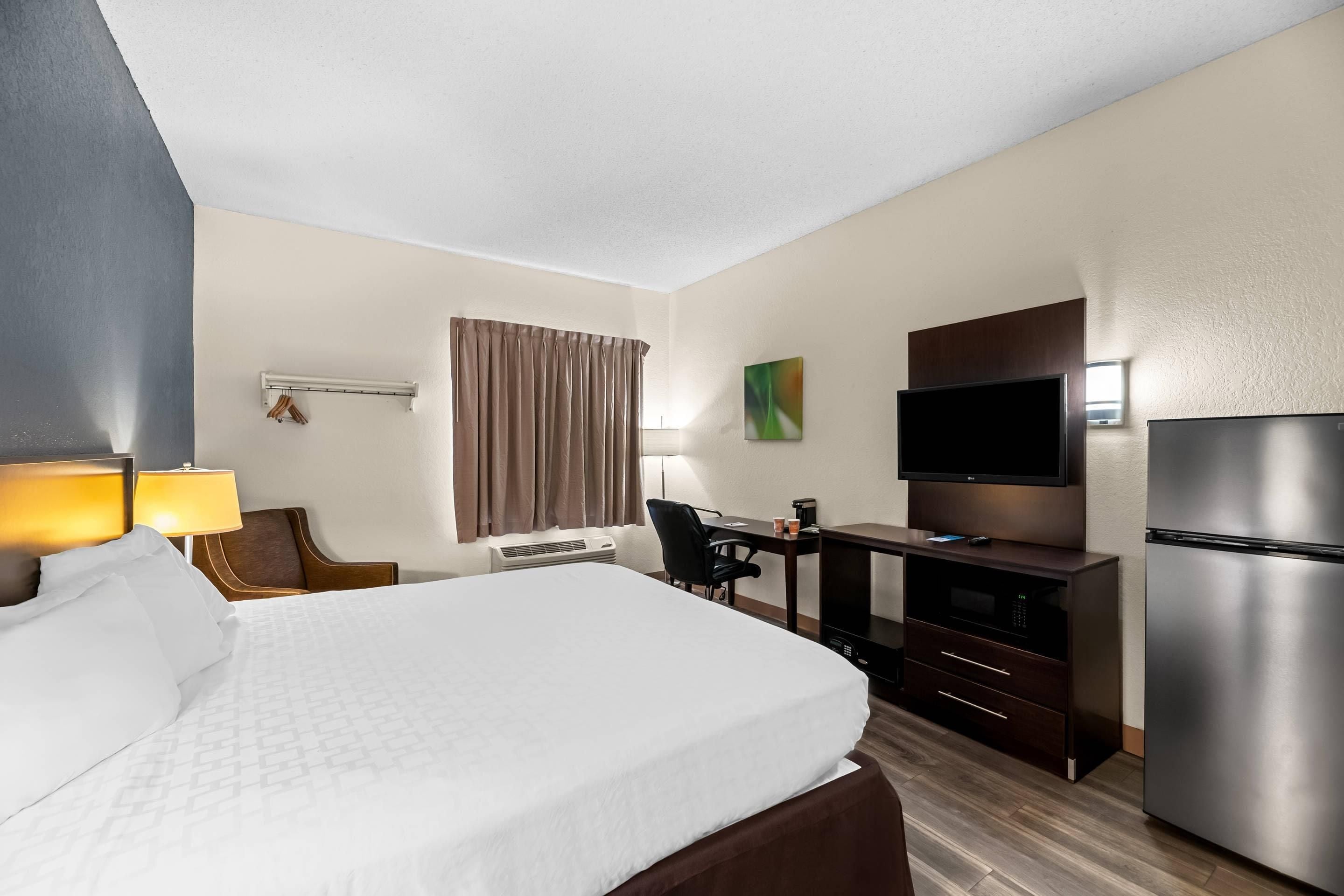 A hotel room with a bed, desk, chair, TV, and refrigerator.