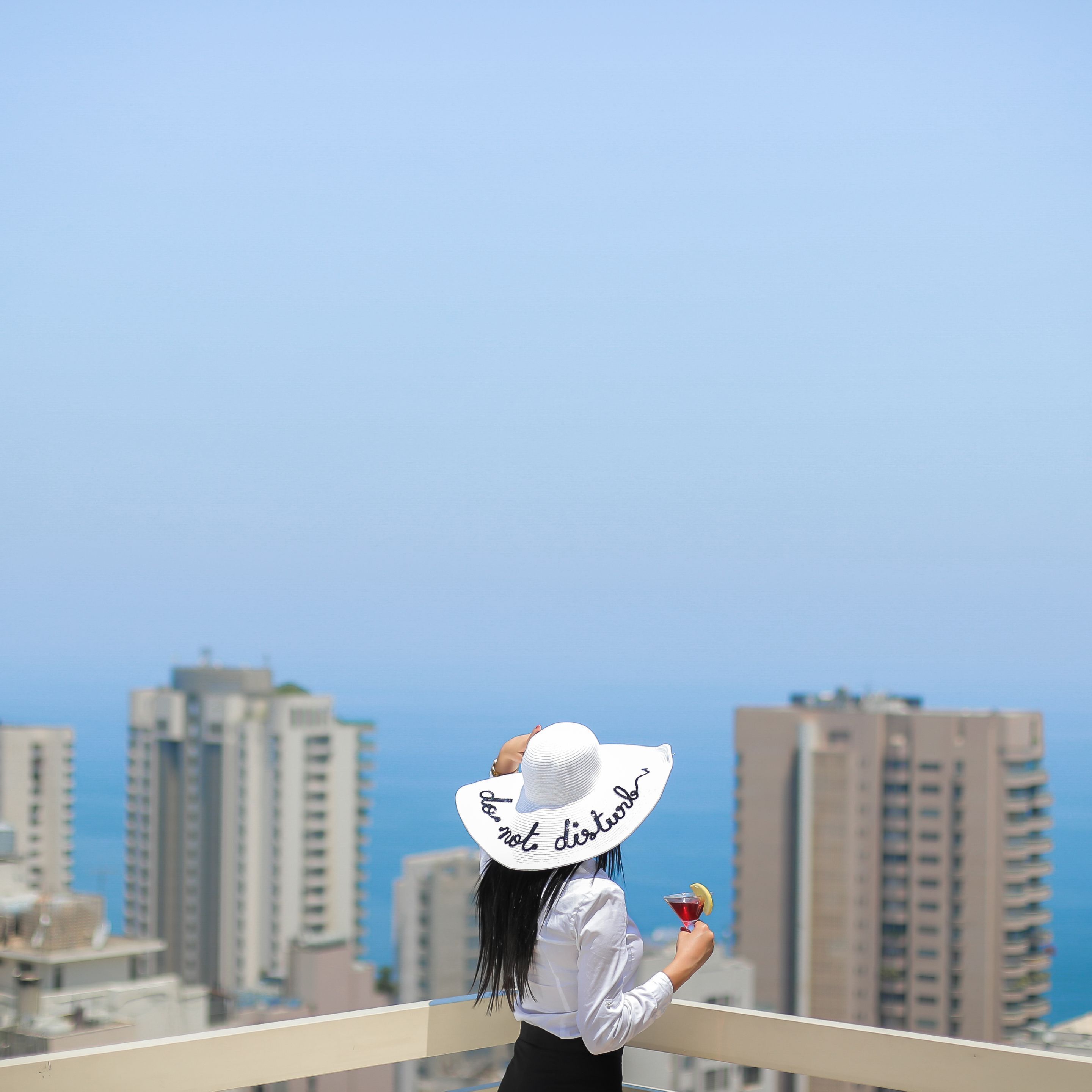 Una persona en un balcón con vistas a un paisaje urbano con edificios altos y cielo despejado.