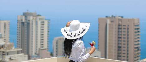 Una persona en un balcón con vistas a un paisaje urbano con edificios altos y cielo despejado.