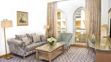 A living room with a patterned sofa, a glass coffee table, a blue armchair, and a decorative vase with flowers.
