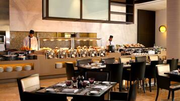 Un comedor moderno con varias mesas y sillas, un mostrador de buffet y una zona de cocina con chefs.