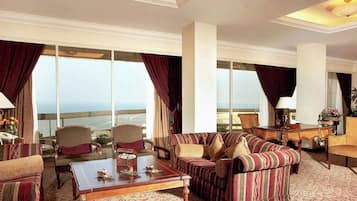 Un salón amplio con un sofá grande, sillones y una mesa de centro. La habitación tiene ventanas grandes con cortinas, que ofrecen vistas al océano.
