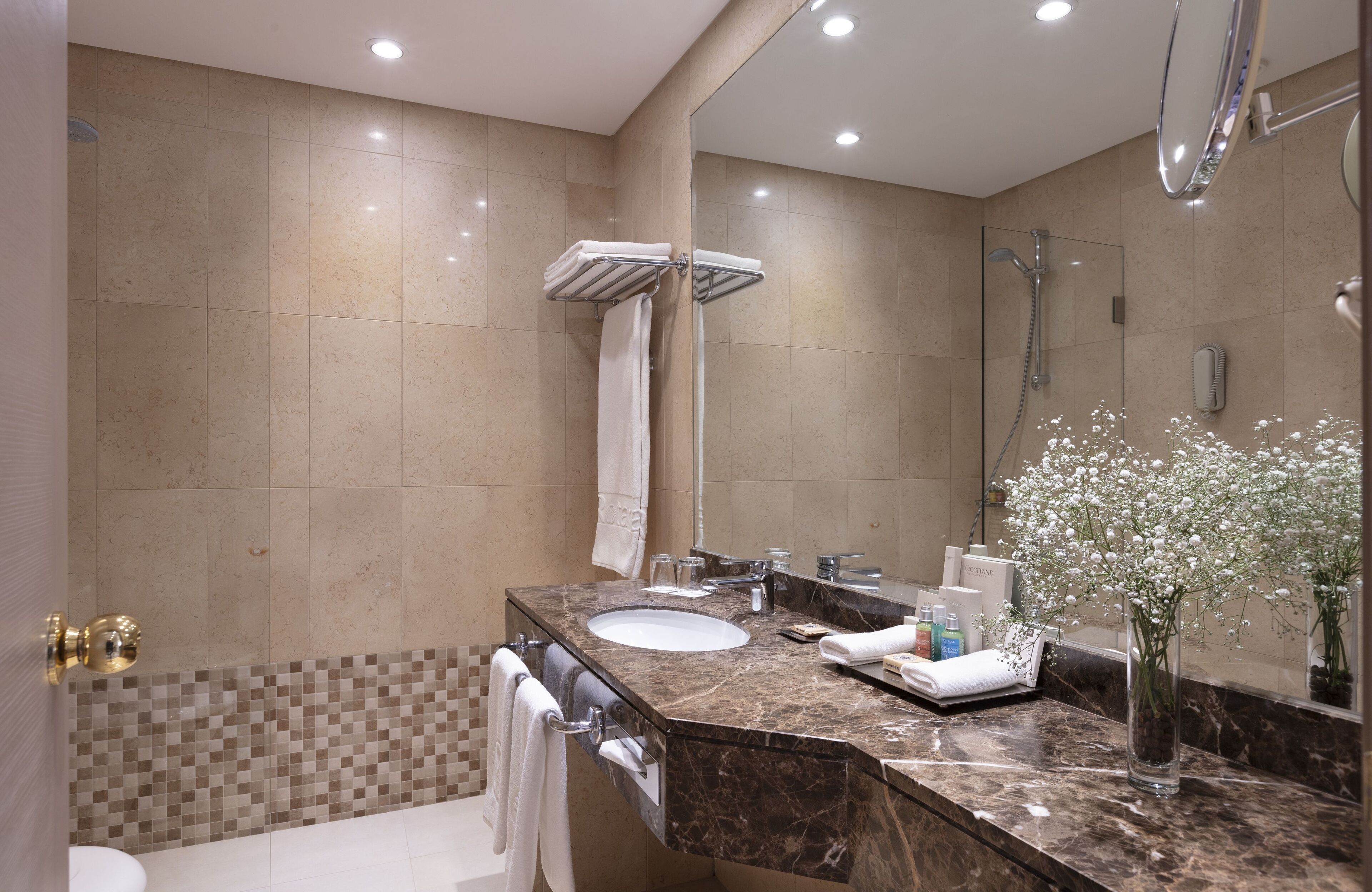 Un baño moderno con lavamanos de mármol, cabina de ducha de vidrio y un espejo grande.