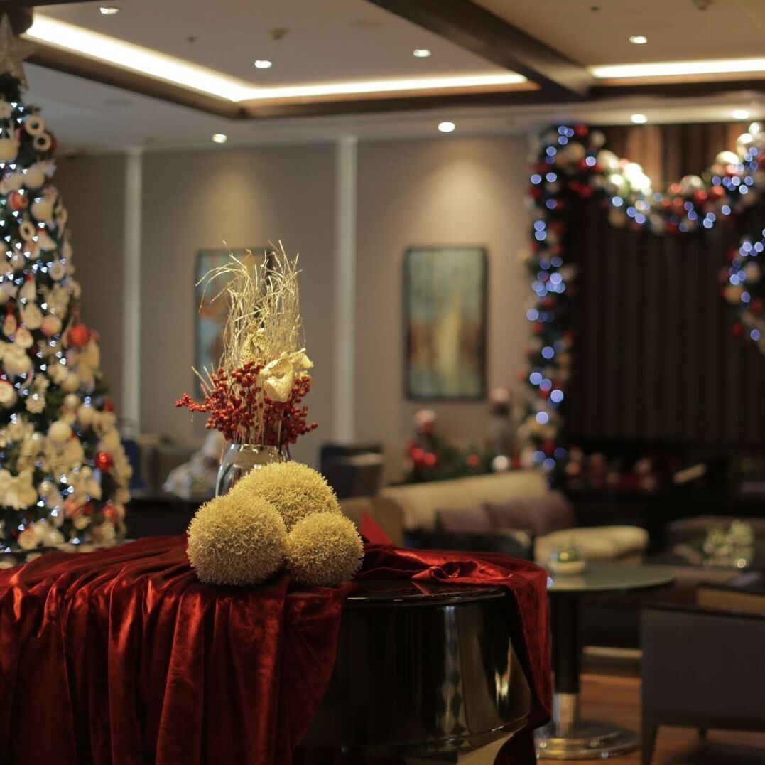 A hotel lobby with a Christmas tree, a vase with dried flowers, and a red velvet-covered table.